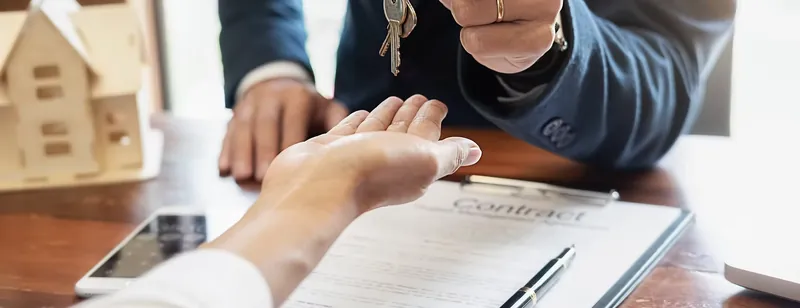 An estate agent handing over paperwork beside a model house